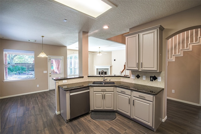 kitchen featuring sink, kitchen peninsula, stainless steel dishwasher, dark wood-type flooring, and dark stone countertops