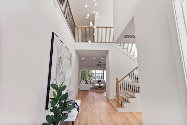 entryway featuring ceiling fan with notable chandelier, a towering ceiling, and light hardwood / wood-style flooring