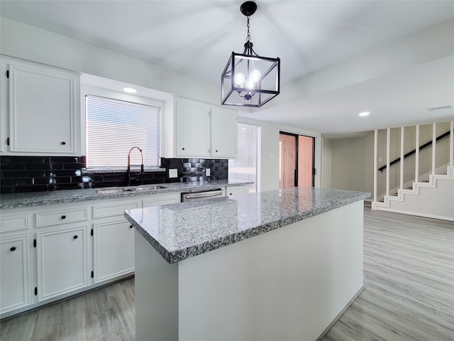 kitchen featuring backsplash, sink, a center island, light wood-type flooring, and white cabinetry