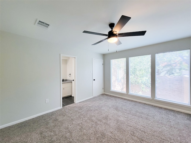 unfurnished bedroom with ceiling fan, dark colored carpet, and ensuite bath