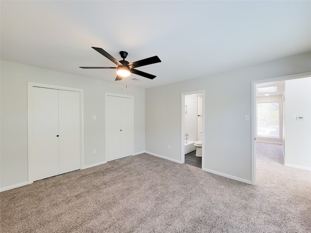 unfurnished bedroom featuring ceiling fan, multiple closets, carpet flooring, and ensuite bath