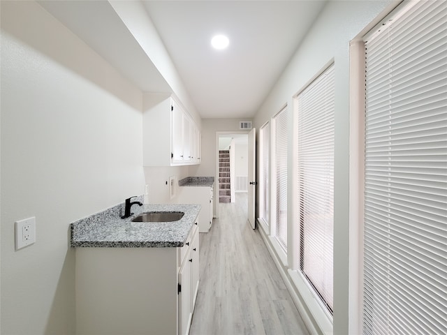 kitchen with washer / dryer, sink, light wood-type flooring, white cabinets, and light stone counters