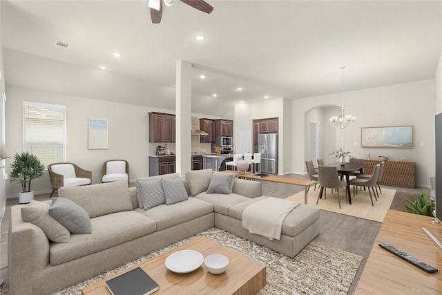 living room featuring ceiling fan with notable chandelier and light wood-type flooring