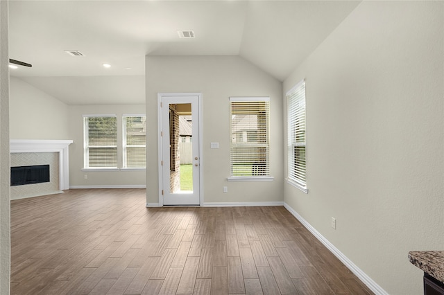 unfurnished living room featuring lofted ceiling, wood-type flooring, a tile fireplace, and plenty of natural light