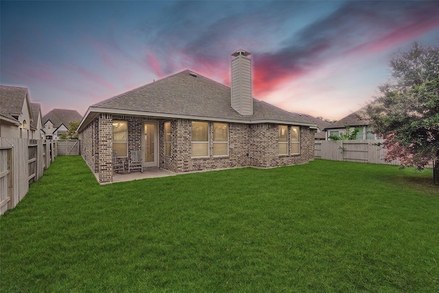 back house at dusk with a patio area and a lawn