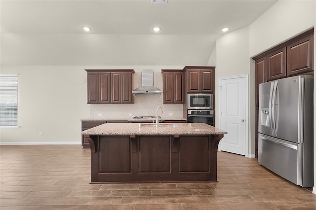 kitchen with appliances with stainless steel finishes, sink, dark brown cabinets, wall chimney exhaust hood, and a kitchen island with sink