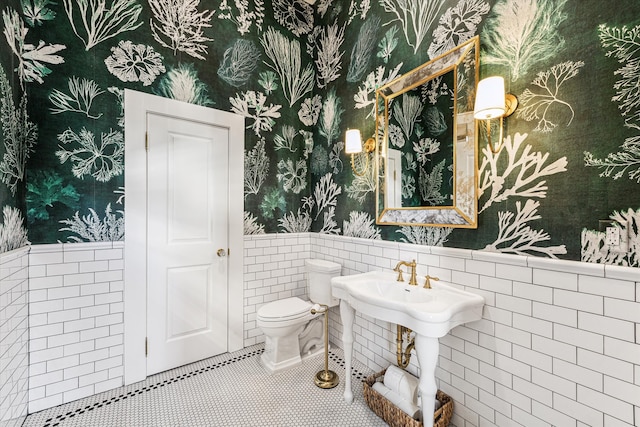 bathroom with toilet, tile patterned floors, and tile walls