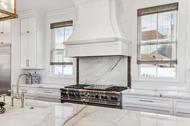 kitchen with high quality appliances, sink, light stone countertops, white cabinetry, and premium range hood