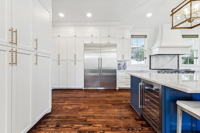 kitchen with appliances with stainless steel finishes, light stone counters, beverage cooler, and dark hardwood / wood-style flooring