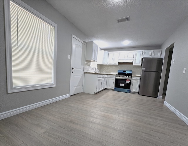 kitchen featuring tasteful backsplash, a textured ceiling, stainless steel appliances, white cabinets, and light hardwood / wood-style flooring