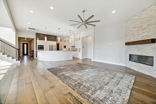 unfurnished living room featuring a stone fireplace, ceiling fan, and dark hardwood / wood-style floors