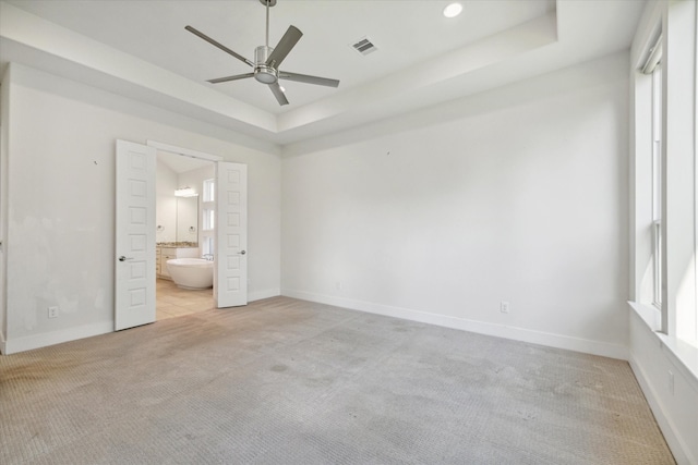 unfurnished bedroom with a tray ceiling, ensuite bath, ceiling fan, and light colored carpet