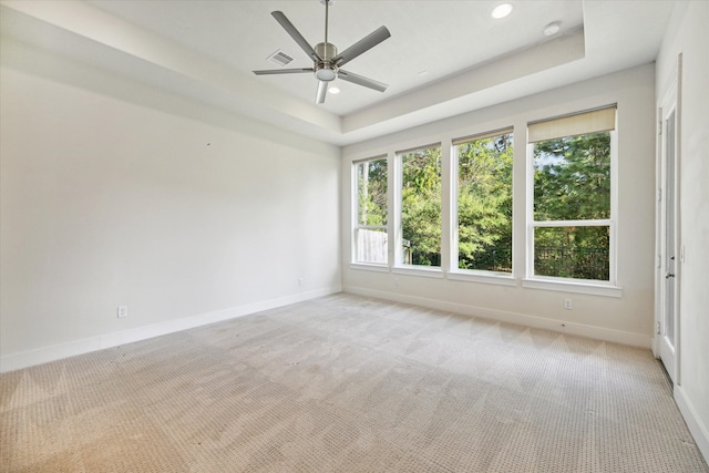 empty room featuring light colored carpet, a raised ceiling, and ceiling fan