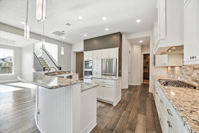 kitchen with a kitchen island with sink, dark wood-type flooring, white cabinets, appliances with stainless steel finishes, and decorative light fixtures