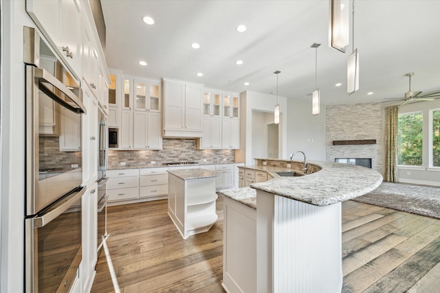 kitchen with light wood-type flooring, sink, pendant lighting, white cabinetry, and an island with sink