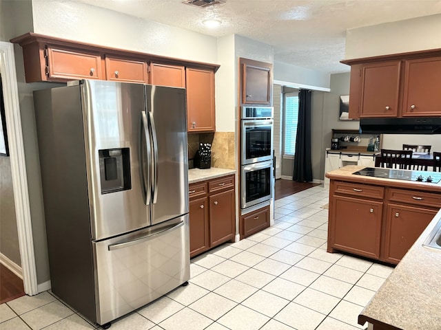 kitchen featuring backsplash, a textured ceiling, stainless steel appliances, extractor fan, and light tile patterned floors