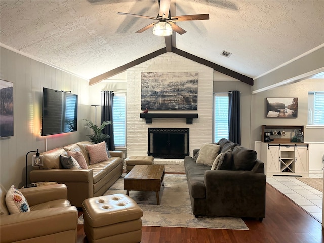 living room with ceiling fan, a textured ceiling, hardwood / wood-style flooring, vaulted ceiling with beams, and a fireplace