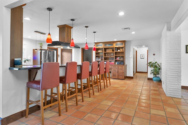 interior space featuring kitchen peninsula, stainless steel fridge, hanging light fixtures, a breakfast bar area, and light tile patterned floors