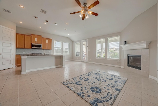 kitchen featuring a wealth of natural light, vaulted ceiling, light tile patterned floors, and a center island with sink