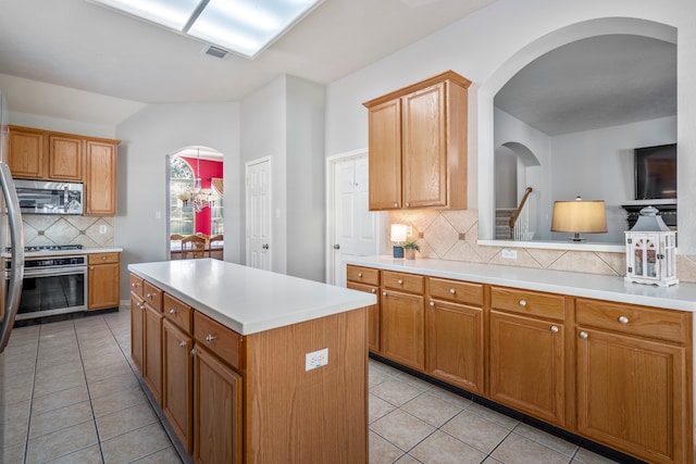 kitchen with a center island, lofted ceiling, tasteful backsplash, light tile patterned flooring, and stainless steel appliances