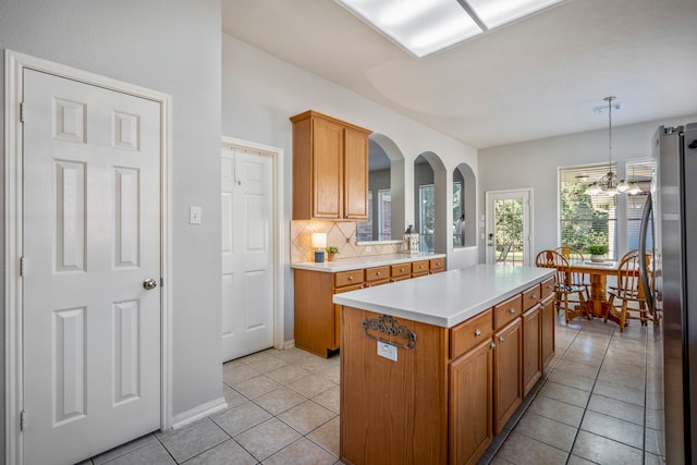 kitchen featuring stainless steel refrigerator, light tile patterned floors, tasteful backsplash, pendant lighting, and a kitchen island