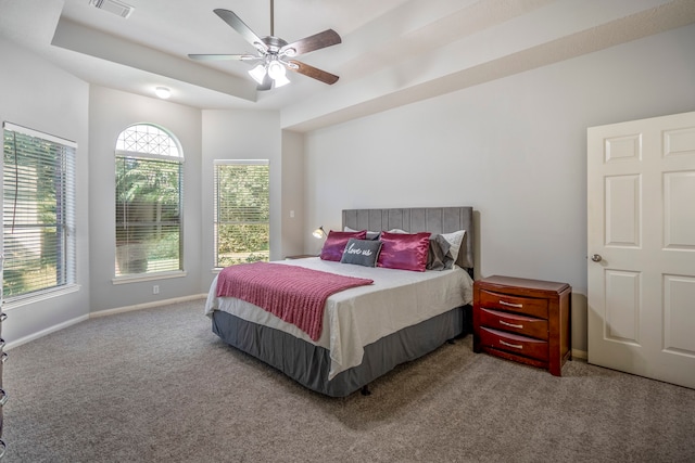 carpeted bedroom with a raised ceiling and ceiling fan