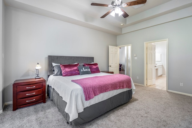 bedroom featuring connected bathroom, light colored carpet, a raised ceiling, and ceiling fan