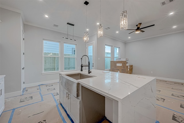 kitchen with decorative light fixtures, an island with sink, sink, ornamental molding, and light stone counters