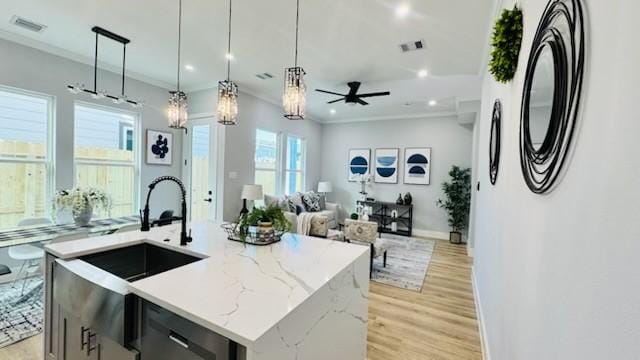 kitchen featuring pendant lighting, black dishwasher, light stone countertops, light hardwood / wood-style floors, and a center island with sink