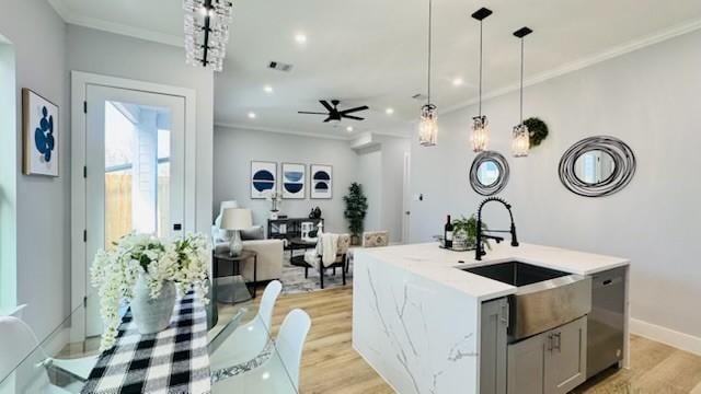 kitchen with gray cabinetry, a center island with sink, ornamental molding, pendant lighting, and light hardwood / wood-style floors