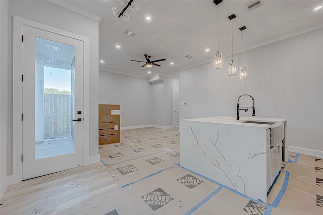 kitchen featuring ceiling fan, a center island with sink, hanging light fixtures, and ornamental molding