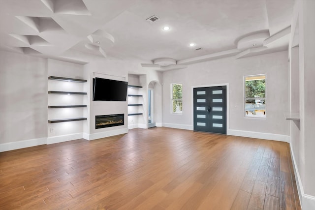 unfurnished living room with built in features, wood-type flooring, a healthy amount of sunlight, and french doors