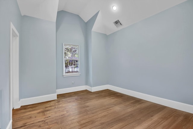 spare room featuring wood-type flooring and vaulted ceiling