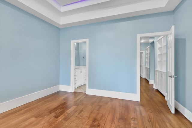 unfurnished bedroom featuring ensuite bath, a raised ceiling, and light wood-type flooring