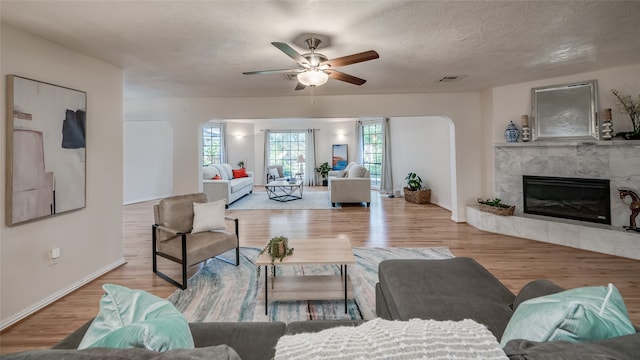 living room featuring a fireplace, a textured ceiling, light wood-type flooring, and ceiling fan