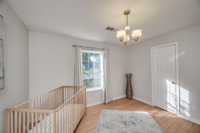 bedroom featuring a notable chandelier, a crib, and light wood-type flooring