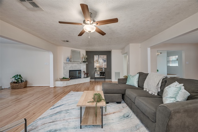 living room featuring a high end fireplace, light hardwood / wood-style flooring, a textured ceiling, and ceiling fan