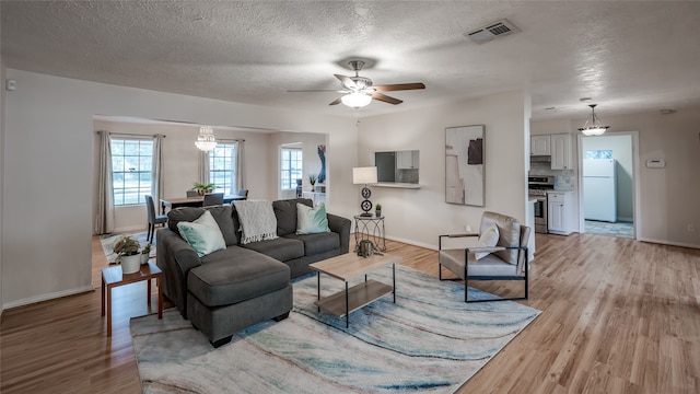 living room with light hardwood / wood-style flooring, a textured ceiling, and ceiling fan