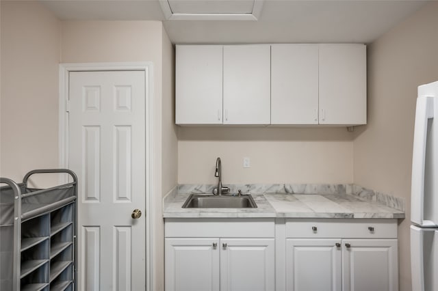 interior space with light stone counters, sink, white refrigerator, and white cabinets