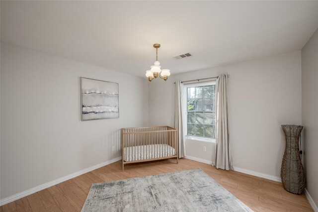 unfurnished bedroom featuring a notable chandelier, wood-type flooring, and a crib