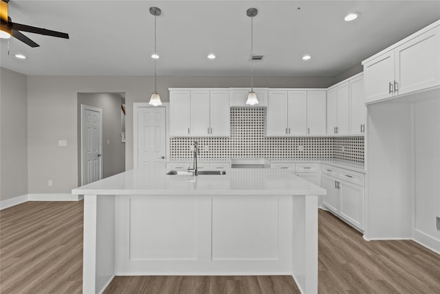 kitchen with light hardwood / wood-style flooring, white cabinets, sink, and hanging light fixtures