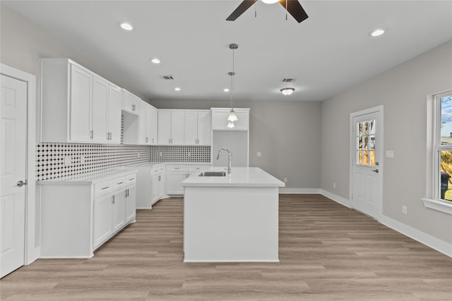 kitchen featuring sink, hanging light fixtures, light hardwood / wood-style floors, white cabinets, and a center island with sink