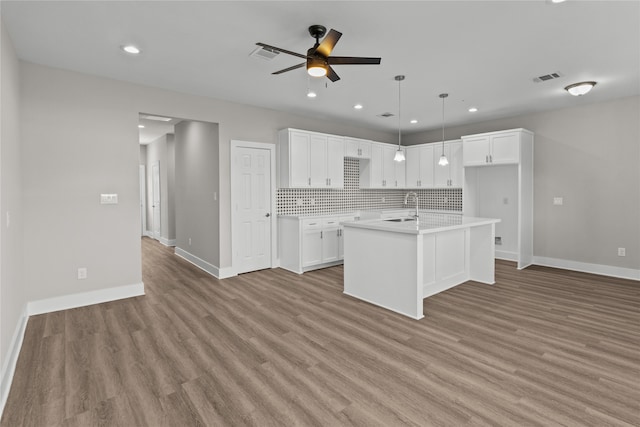 kitchen with a kitchen island with sink, tasteful backsplash, white cabinetry, light hardwood / wood-style floors, and ceiling fan