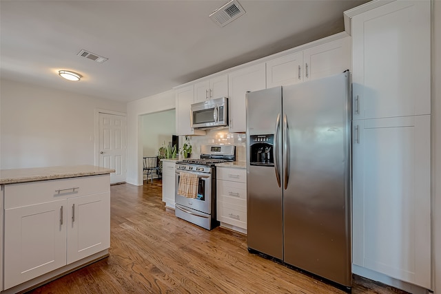 kitchen with decorative backsplash, stainless steel appliances, light stone countertops, white cabinetry, and light hardwood / wood-style floors