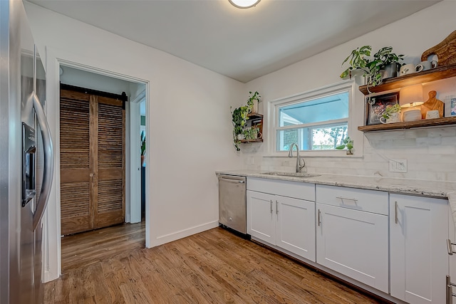 kitchen featuring sink, light stone countertops, white cabinets, light wood-type flooring, and appliances with stainless steel finishes