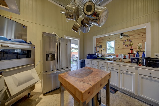 kitchen with stainless steel fridge with ice dispenser, wooden walls, and white cabinets