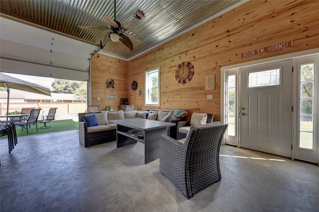 living room with wood walls, a high ceiling, plenty of natural light, and ceiling fan