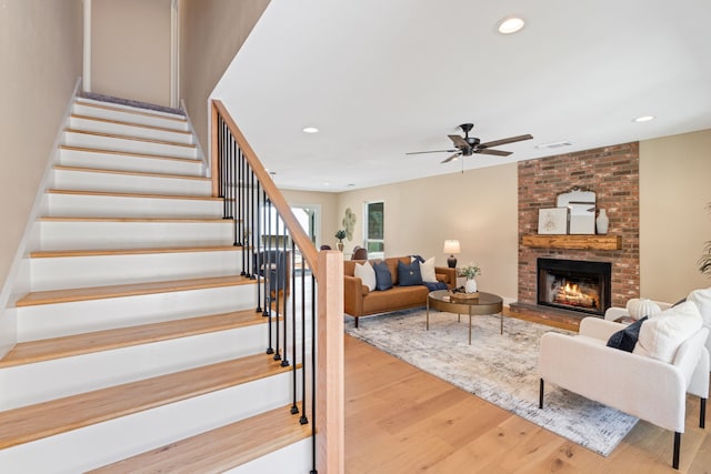 living room with light hardwood / wood-style floors, a large fireplace, and ceiling fan