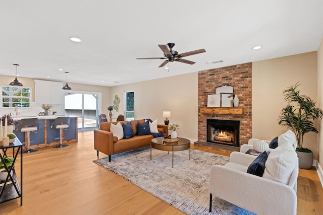 living room with a brick fireplace, light wood-type flooring, and ceiling fan