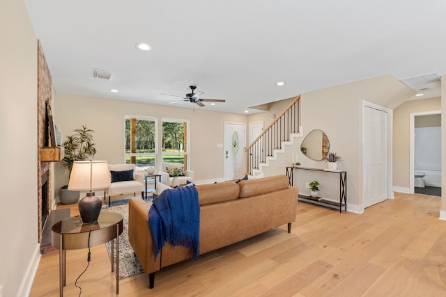 living room featuring light hardwood / wood-style flooring, a large fireplace, and ceiling fan